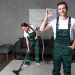 smiling young cleaning company workers using vacuum cleaner and showing ok sign